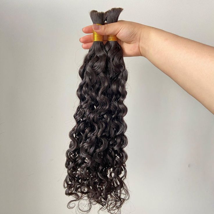 Curly bulk  hair extensions held by a hand against a plain background 