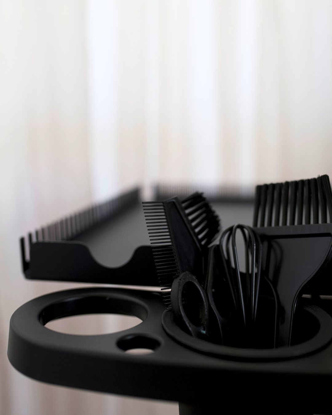 Black hairdressing tools including scissors and combs on a stand with a blurred background