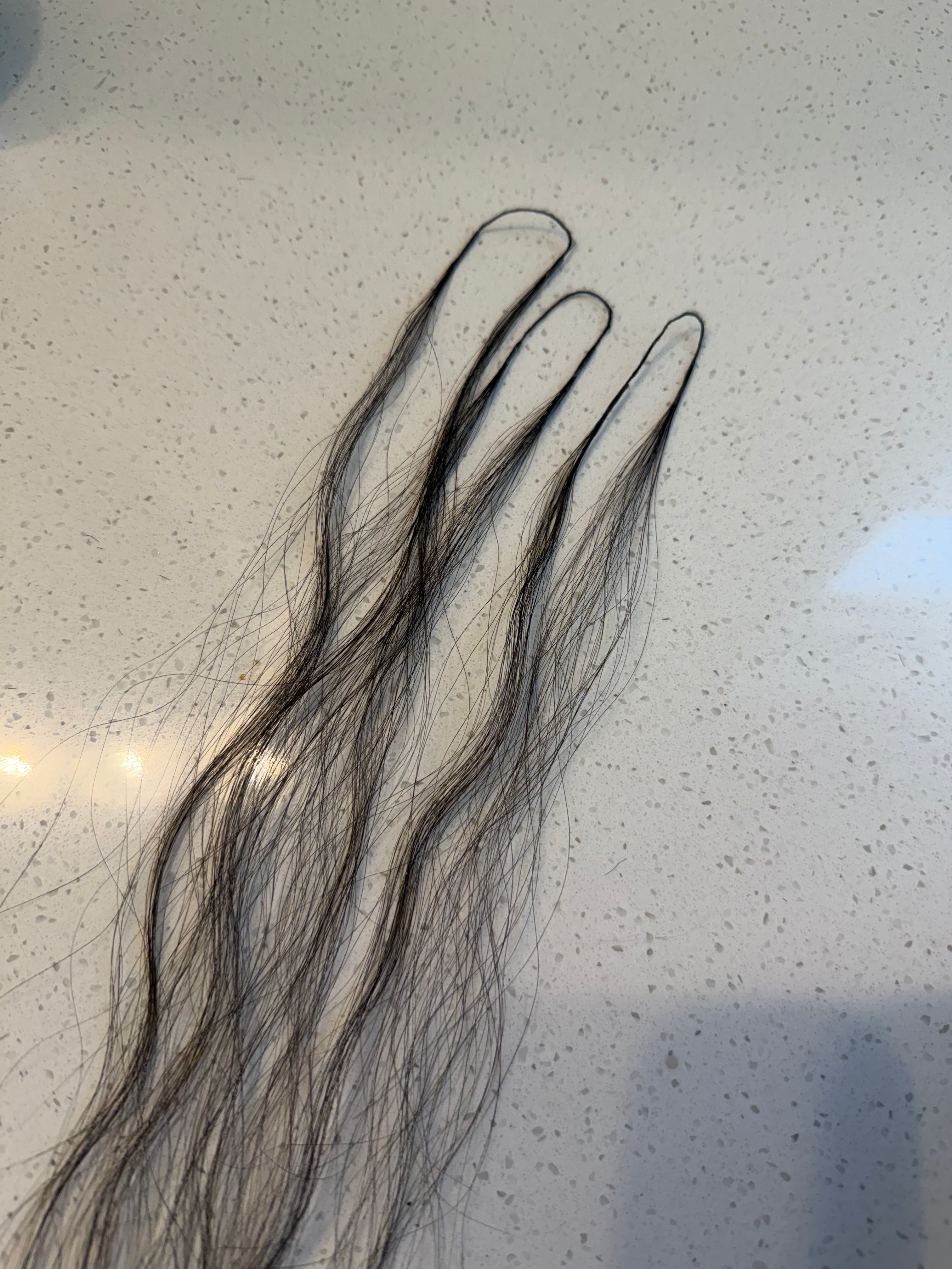 Three black crochet hair strands on a speckled gray surface